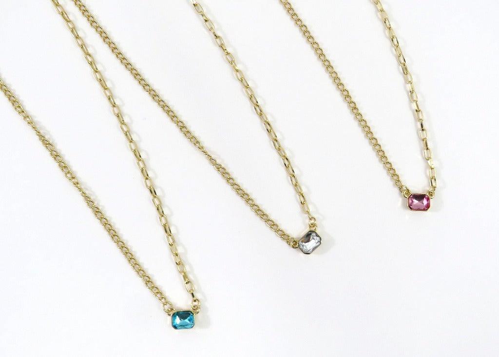 3 necklaces side by side with gold chains that have 2 different styles and bright faux stone crystals in teal, white and pink