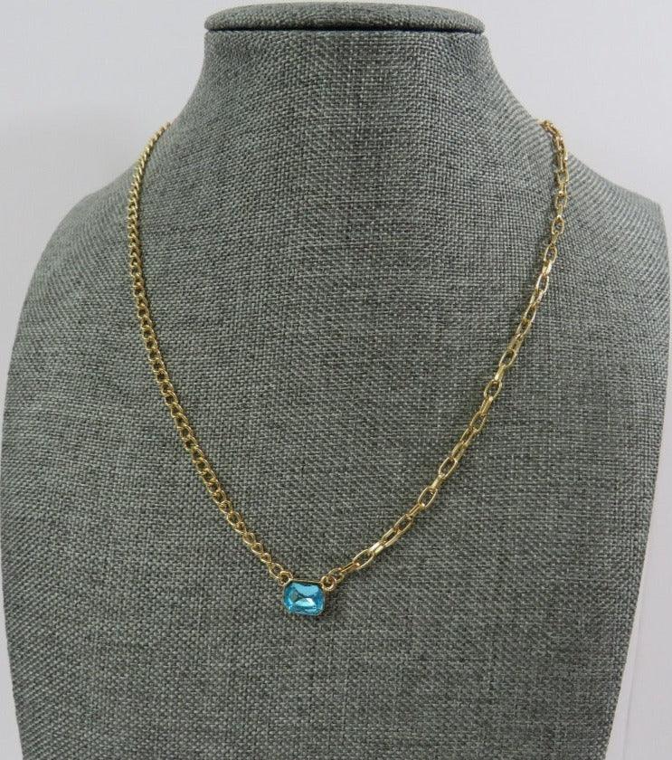 bright stone necklace in teal with gold chains of 2 different styles on a necklace mannequin on a white background