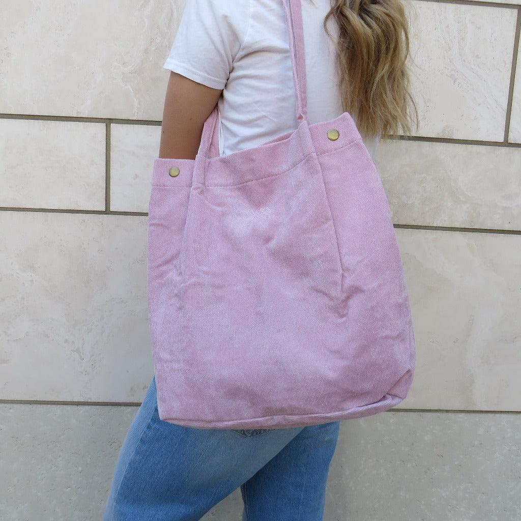 Light pink bella corduroy carry all carried on the shoulder of a person in a white shirt and jeans 