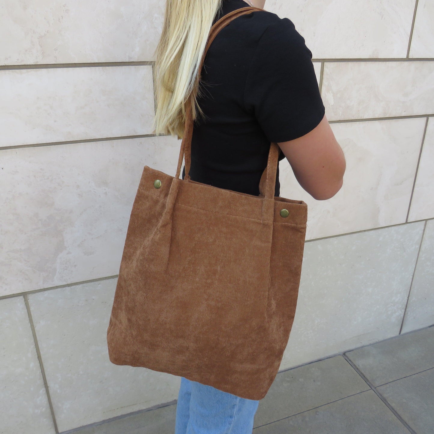 Brown bella corduroy carry all carried on the shoulder of a person in a black shirt and jeans 