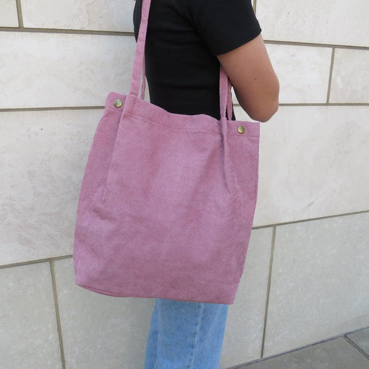 Pink bella corduroy carry all carried on the shoulder of a person in a black shirt and jeans 