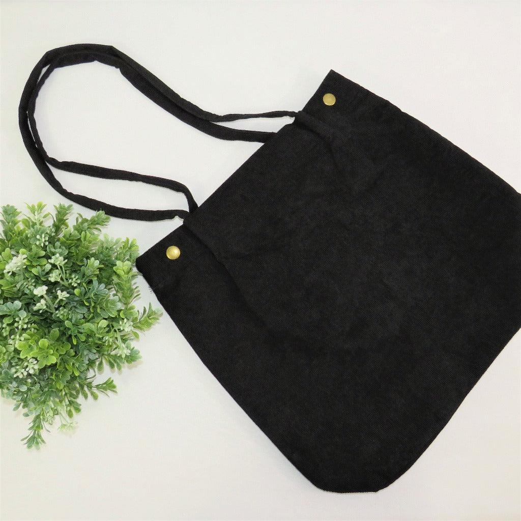 Black bella corduroy carry all bag on the white background next to some greenery