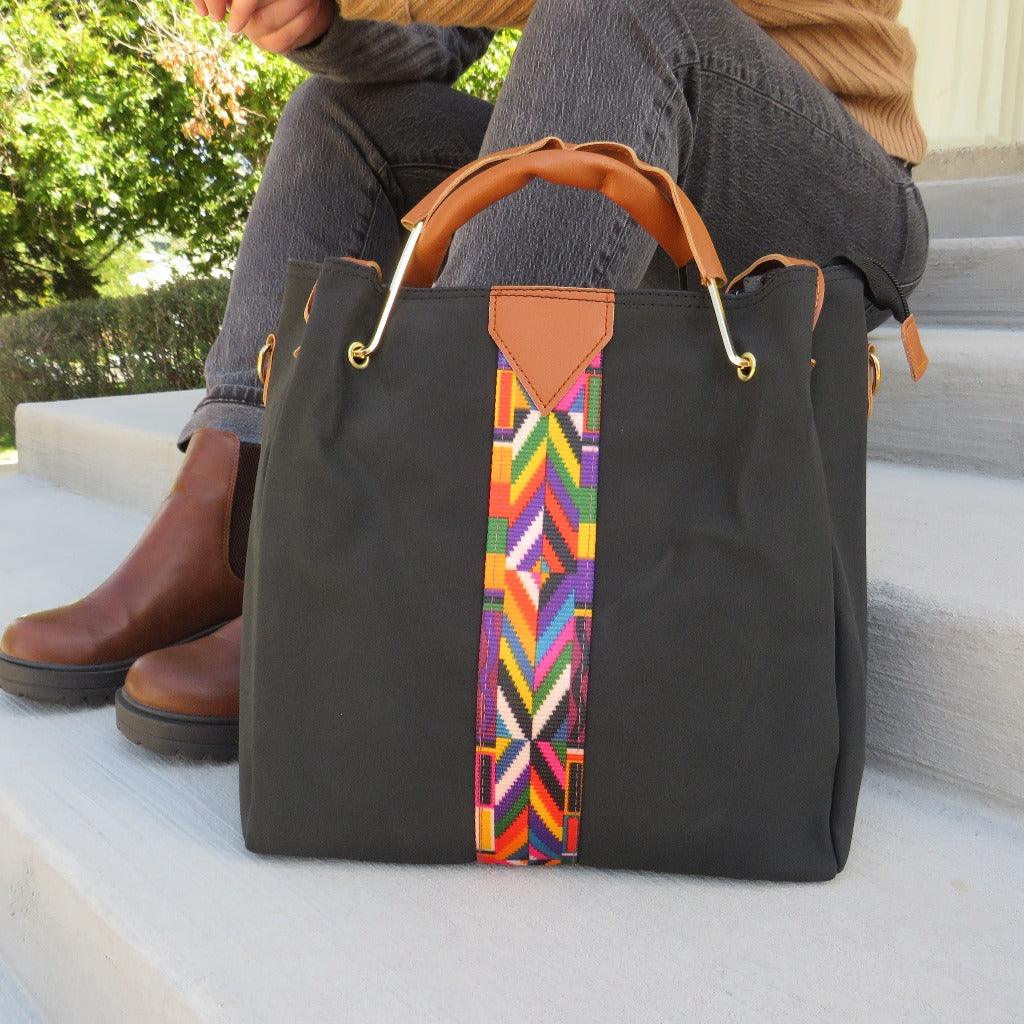 the chole carry all purse with camel handles and multicolor geometric stripe detail placed on stairs next to a women in black jeans and a sweater