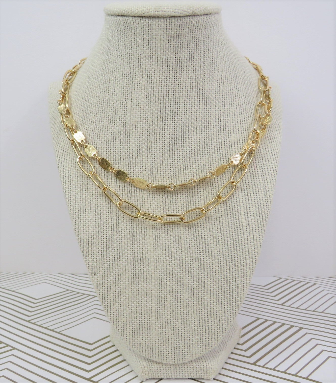 Double layer gold necklace with 2 styles of chains on a gray, tan and gold decorated background