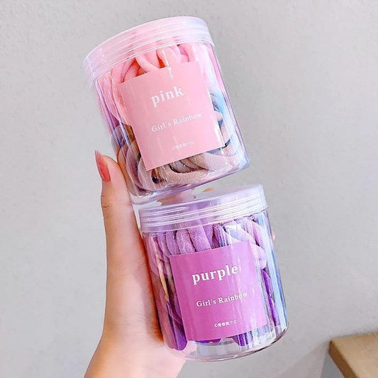 Pink and purple nylon hair ties in clear plastic container being held up by one hand. Each container has 2 colors of pink and purple