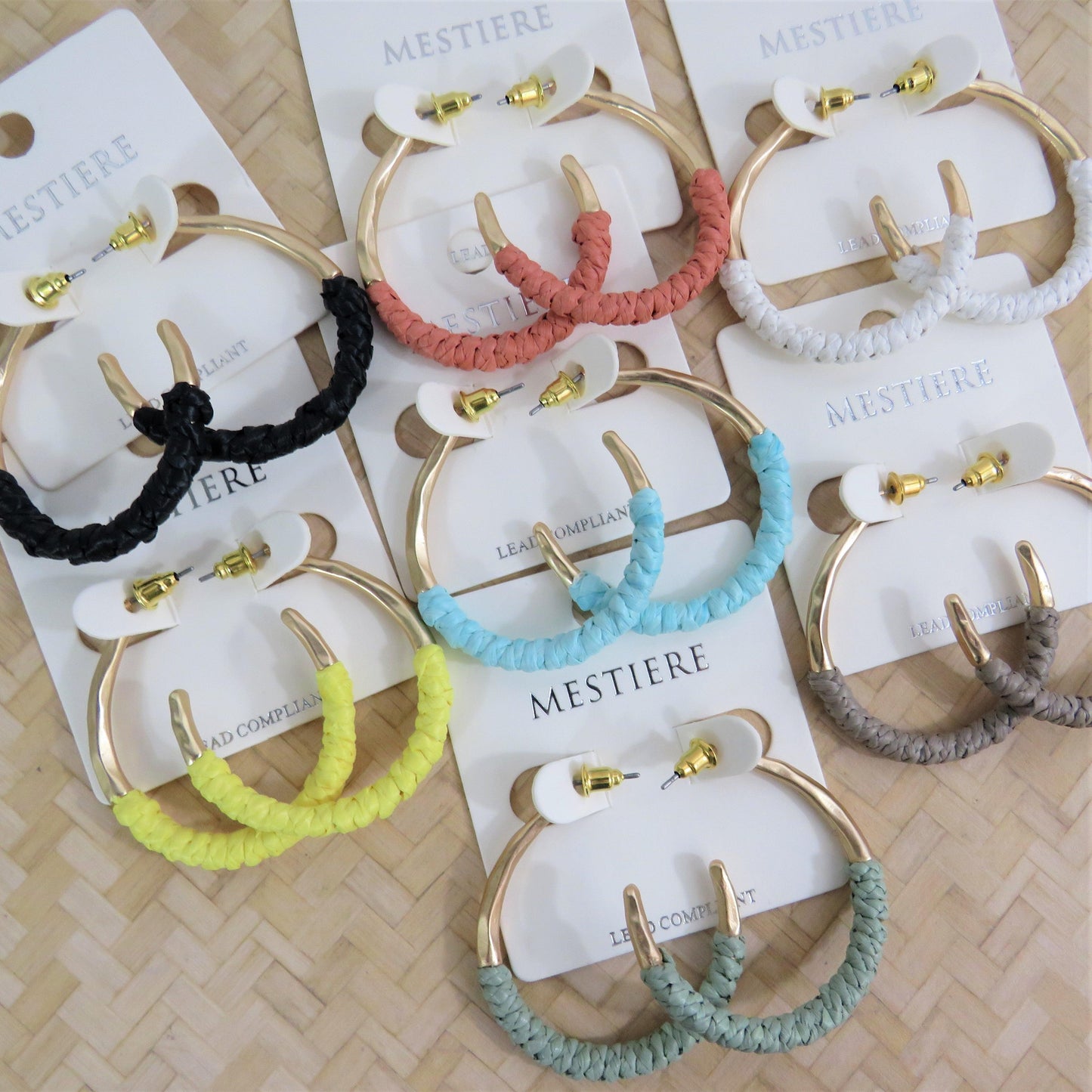 7 pair of rattan wrapped gold hoops in several colors on a rattan back ground