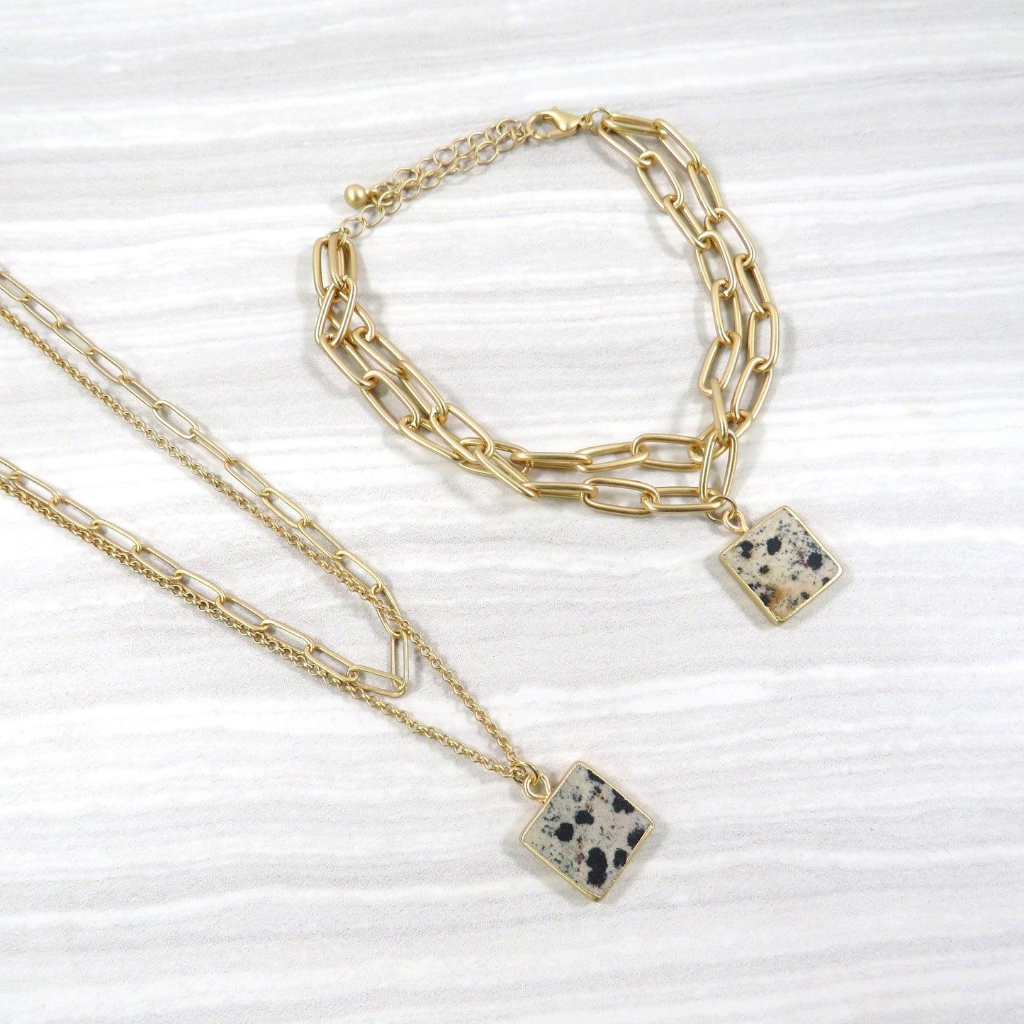 double layer gold chain necklace and bracelet set with a square Dalmatian jasper stone on a gray and white tile background