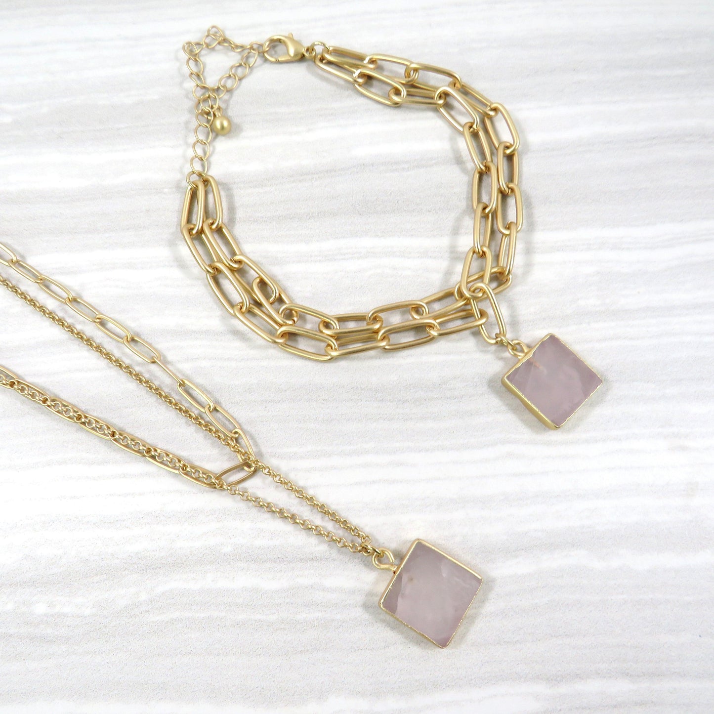 double layer gold chain necklace and bracelet set with a square rose quartz stone on a gray and white tile background