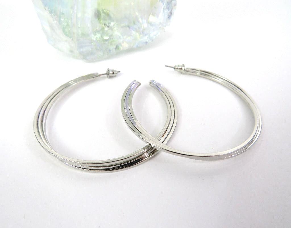 silver layered hoop with post backs on a white background next to a clear crystal